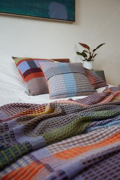 a bed topped with lots of pillows next to a potted plant