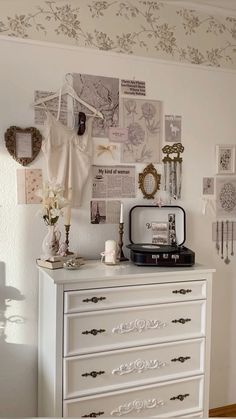 a white dresser topped with lots of drawers next to a wall covered in pictures and photos