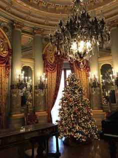 a christmas tree is in the middle of a room with chandeliers and curtains