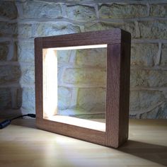 a wooden frame sitting on top of a table next to a brick wall with a light coming through it