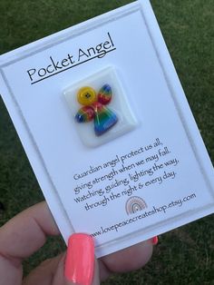 a person holding up a card with a button on it that says pocket angel in front of them