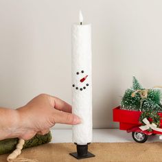 a hand holding a white candle with a snowman face on it next to a red wagon