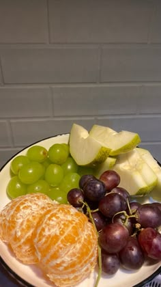 a plate with grapes, oranges and other fruit on it sitting on a table