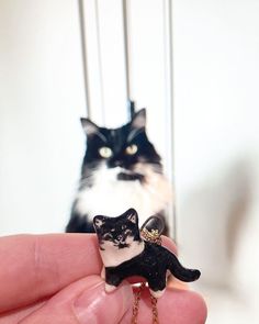 a hand holding a tiny black and white cat on a keychain with a chain attached to it