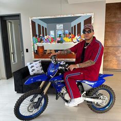 a man sitting on top of a blue dirt bike in front of a large painting