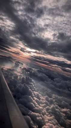 the wing of an airplane as it flies through the sky with clouds and sun rays