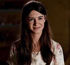 a woman with long brown hair and blue eyes smiles at the camera while wearing a floral shirt