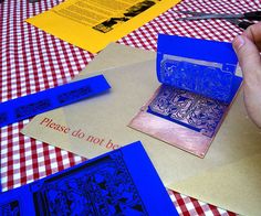 a person cutting out some blue paper on top of a red and white checkered table cloth