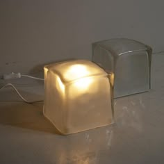 two square shaped lights sitting next to each other on the floor in front of a white wall