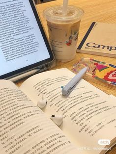 an open book sitting on top of a wooden table next to a laptop computer and a cup of coffee