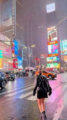 a woman walking across a street in the middle of a busy city at night time