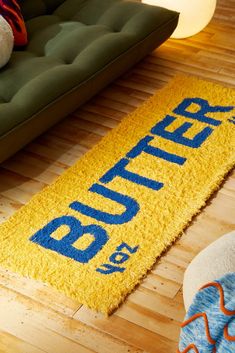 a yellow rug with the word butter on it in front of a green couch and white teddy bear