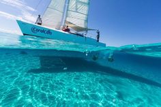 two people on a sailboat in the ocean with clear blue water and bright sunlight