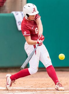 a woman hitting a baseball with a bat and ball in front of her on the field