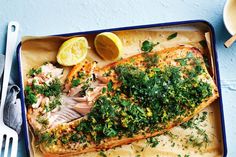 fish with herbs and lemons on a blue tray next to a fork, knife and spoon