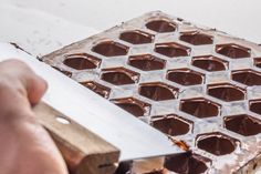 a person is cutting chocolate into squares with a large metal object in the foreground