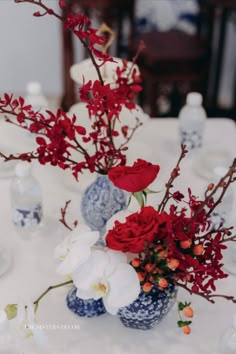 two blue and white vases with red flowers in them sitting on a table cloth