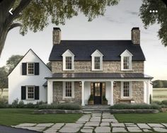 a white house with black shutters on the front and side windows is surrounded by green grass