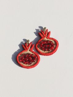 red and gold beaded earrings on a white surface with clippings to the side