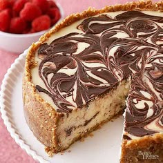 a cheesecake with chocolate and raspberries is on a plate next to a bowl of strawberries