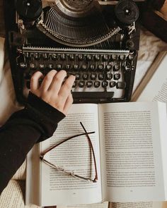 someone is typing on an old fashioned typewriter and reading a book with their hands