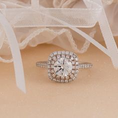 an engagement ring with a diamond center surrounded by white ribbon and lace on a beige background