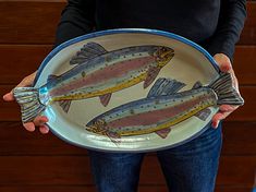 a person holding a plate with two fish on it's front and back sides