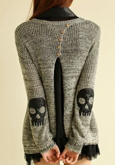 a woman wearing a sweater with skulls on the side and buttons at the back, standing in front of a white wall