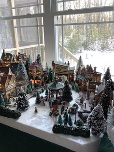 a christmas village set up on a window sill in front of a large window