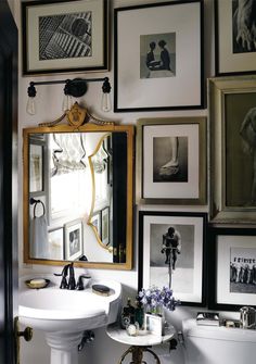 a white sink sitting under a bathroom mirror next to a wall filled with framed pictures