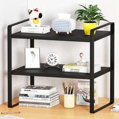 a black shelf with books, magazines and plants on it next to a white wall