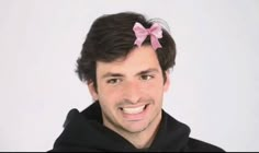 a man with a pink bow on his head and black hoodie smiling at the camera