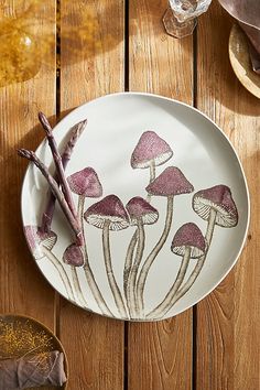 a plate with mushrooms painted on it sitting on a wooden table next to some wine glasses