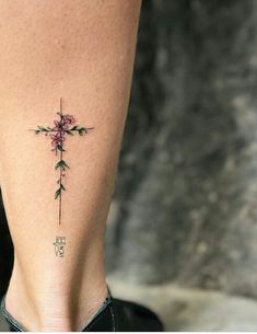 a cross tattoo on the back of a woman's lower leg, with pink flowers