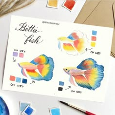 some watercolors are on the table and there is a card with different colored fish