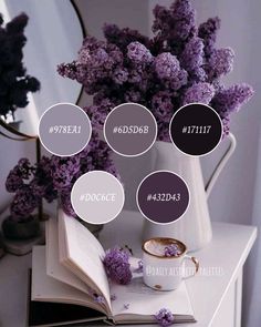 purple flowers in a white vase on top of a table next to an open book