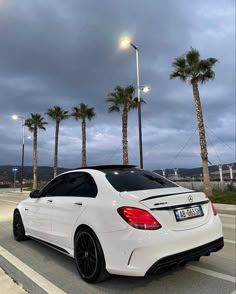 a white mercedes cla parked on the side of the road with palm trees in the background