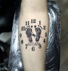 a black and white photo of a clock with two baby feet on it's arm