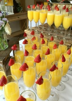 glasses filled with yellow liquid and strawberries on a table