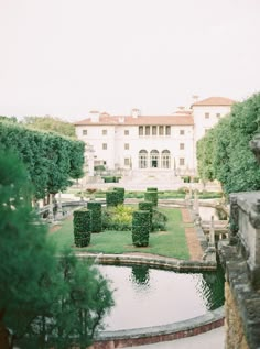 a large white building sitting next to a lush green park filled with lots of trees