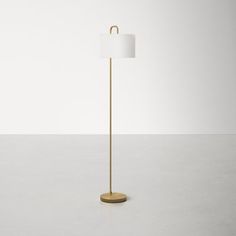 a floor lamp with a white shade on it's side and a gold base