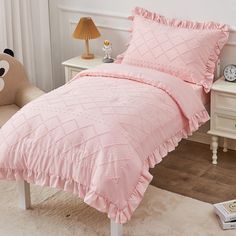 a bed with pink comforter and pillows in a room next to a teddy bear