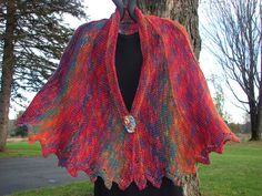 a woman wearing a red and blue shawl standing next to a tree in the grass