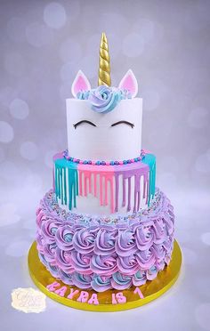 a three tiered birthday cake decorated with icing and a unicorn horn on top