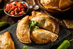 several different types of food on a wooden table with salsa and tortilla shells