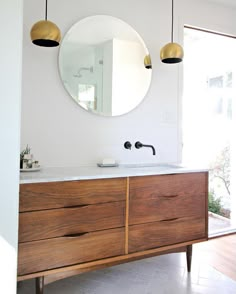 a bathroom vanity with two lights hanging above it and a round mirror on the wall