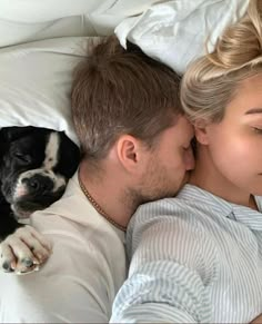 a man and woman laying in bed next to a dog