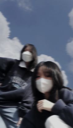 two people with masks on their faces in front of some clouds and blue skys