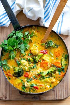 a pan filled with curry and vegetables on top of a cutting board next to a wooden spoon