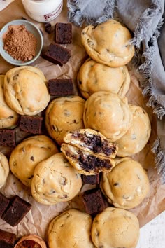 chocolate chip cookies and other desserts are arranged on a piece of parchment paper next to cups of cocoa powder